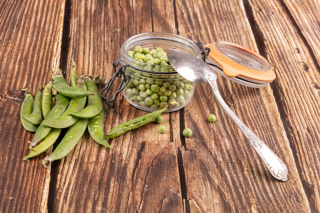 Pois décortiqués dans un bocal en verre avec les cosses sur le côté sur une table en bois