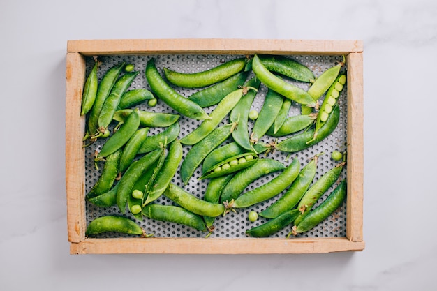 Pois frais dans un plateau en bois sur un fond en marbre, plat poser, vue de dessus