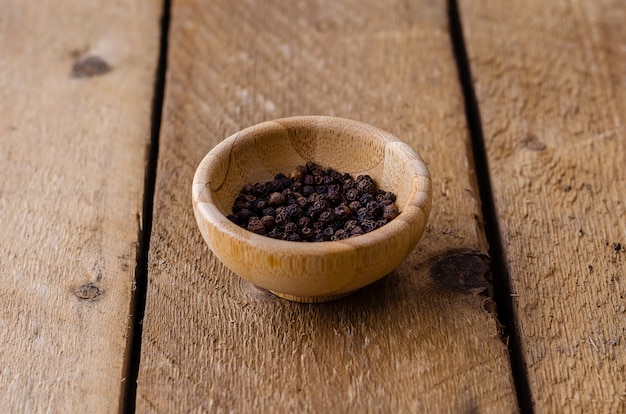 Pois poivre noir dans un bol en bambou sur un fond en bois rustique.