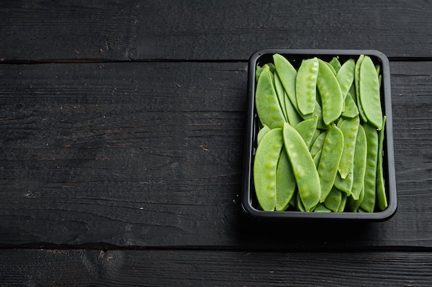 Pois sucré vert biologique prêt à manger, dans un récipient en plastique, sur bois noir