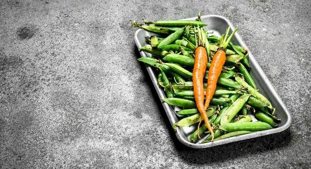 Pois verts aux carottes sur un plateau en acier.