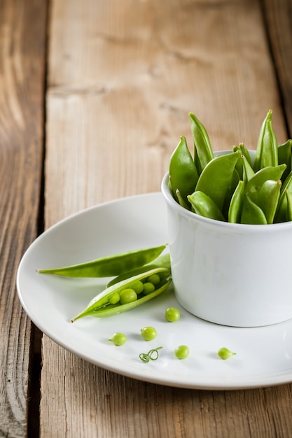 Pois verts en gousses en plaque blanche sur table en bois