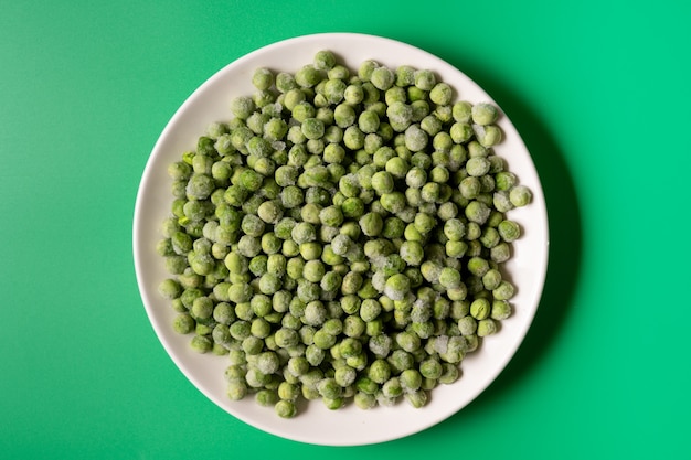 Pois verts surgelés dans un bol sur fond vert, pose à plat.