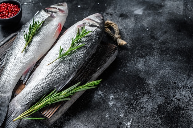 Poisson de bar cru sur une planche à découper avec des épices, des herbes. Fond noir. Vue de dessus. Copiez l'espace.