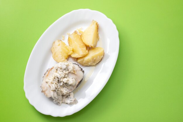 Poisson bouilli avec sauce tartare et pomme de terre bouillie sur plat blanc sur table verte