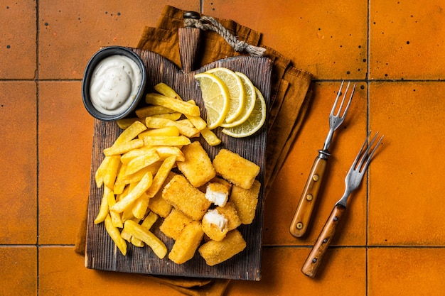 Poisson et chips Fast-food britannique Poisson-bâton avec frites sur planche en bois Arrière-plan orange Vue du haut