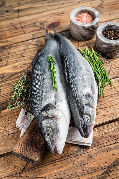 Poisson cru frais de bar sur une planche à découper en bois avec du romarin. fond en bois. Vue de dessus.