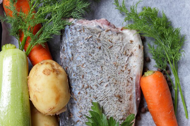 Poisson cru avec légumes épices et herbes avant cuisson sur papier sulfurisé Gros plan de carpe argentée fraîche