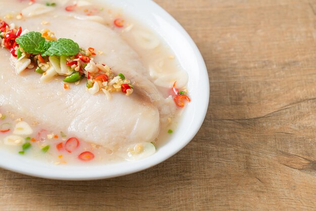 Poisson cuit à la vapeur dans une sauce épicée au citron on white plate