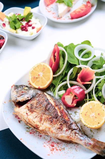 Poisson cupra dorade frit sur plaque blanche avec roquette de jardin d'oignons et tranches de citron