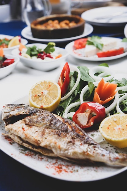 Poisson cupra dorade frit sur plaque blanche avec roquette de jardin d'oignons et tranches de citron