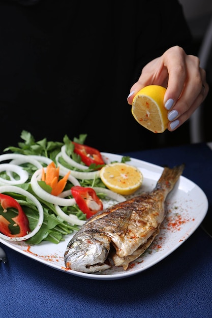 Poisson cupra dorade frit sur plaque blanche avec roquette de jardin d'oignons et tranches de citron