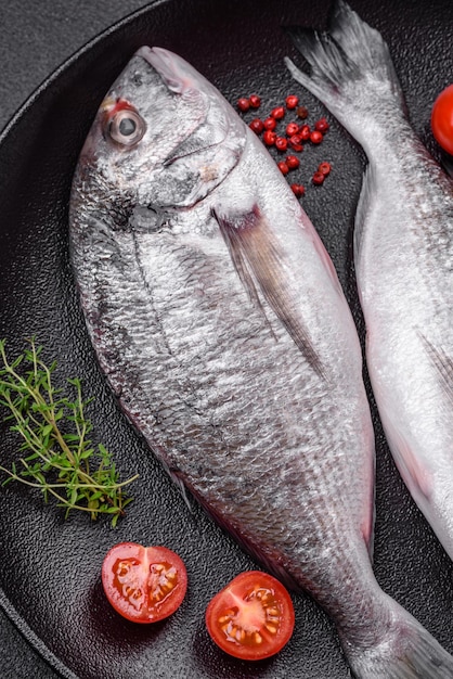 Poisson dorada cru frais avec des épices et des herbes salées sur fond de béton foncé