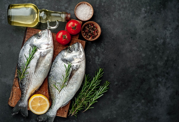 Poisson dorade cru aux épices et ingrédients tomate, razmorine, huile de tournesol, citron sur un fond de pierre avec espace de copie pour votre texte