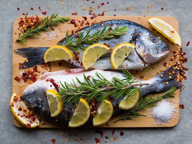 Poisson dorade ou dorade frais non cuit avec des tranches de citron, des épices, des herbes et du romarin sur une planche à découper. Cuisine méditerranéenne. Vue de dessus