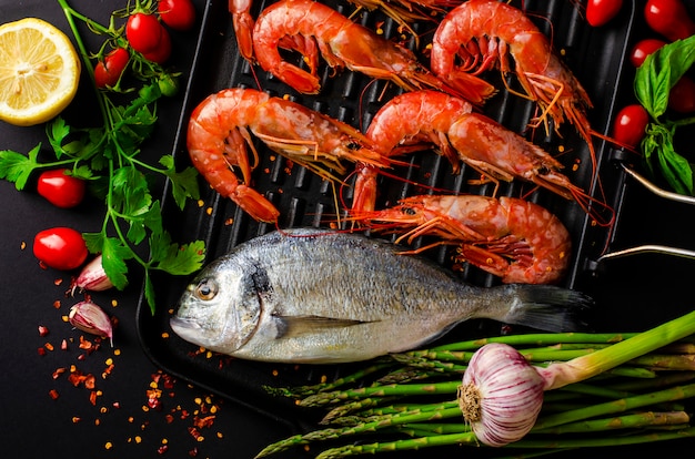 Poisson dorado frais et crevettes tigrées sur une lèchefrite en fer et légumes pour la cuisson