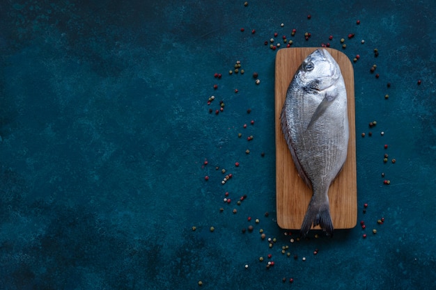 Poisson dorado frais sur une planche à découper en bois sur une table bleue