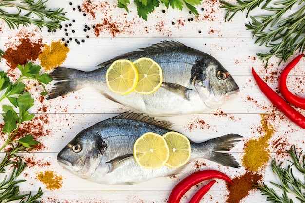 Photo poisson dorado frais, romarin et épices autour sur une table en bois blanche.