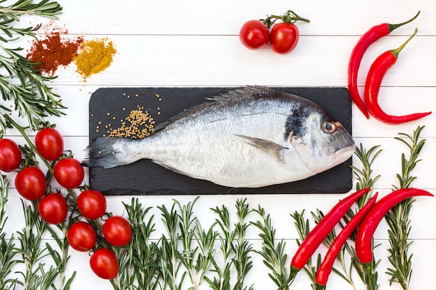 Poisson dorado frais, romarin, tomates cerises, poivre froid sur une table en bois blanc. Vue de dessus.