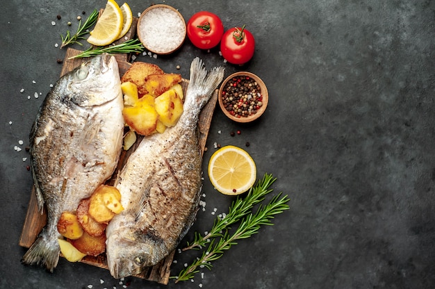 poisson dorado frit et pommes de terre frites sur une planche à découper avec des épices et du citron sur un fond de pierre avec copie espace pour votre texte