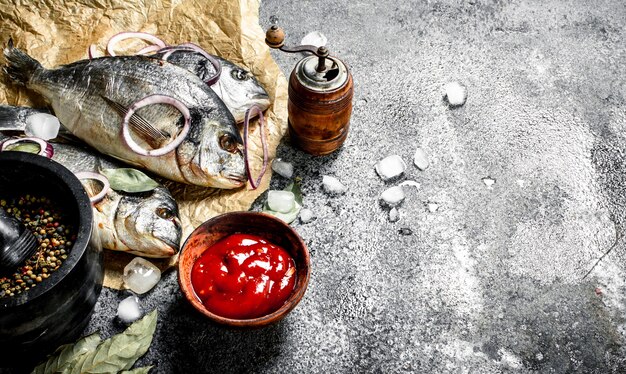 Poisson Dorado non préparé frais avec sauce et épices sur table rustique.