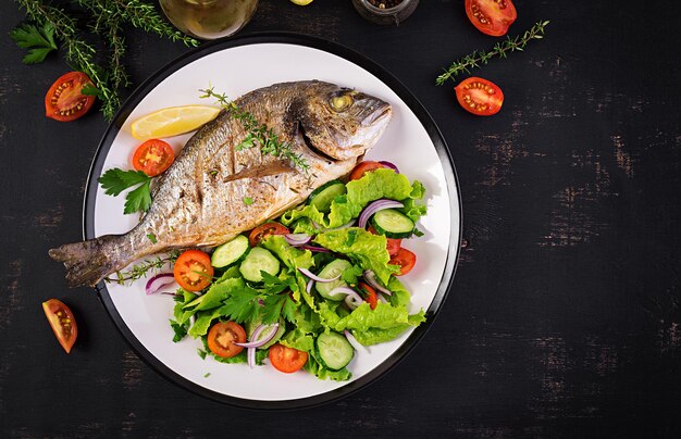 Poisson doré au four avec citron et salade fraîche dans une assiette blanche sur un fond rustique sombre Vue supérieure Dîner sain avec concept de poisson Diète et alimentation propre