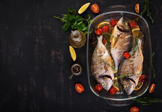 Poisson doré cuit au four avec citron et herbes dans une casserole sur un fond rustique sombre Vue supérieure Dîner sain avec concept de poisson Diète et alimentation propre