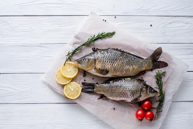 Poisson entier cru frais de carpe miroir avec épices, citron et herbes sur fond de papier parchemin, allongé sur un fond blanc en bois de planches