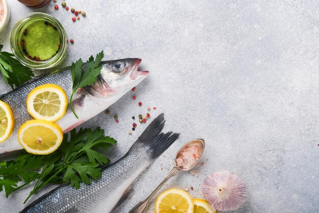 Poisson frais Bar de mer cru avec sel poivre persil huile d'olive et citron sur une planche à découper sur fond rustique en béton gris clair Fond de cuisine alimentaire Vue de dessus espace de copie