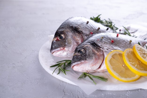 Poisson frais de dorade crue décoré de tranches de citron, herbes sur fond gris. Concept d'aliments sains, vue de dessus, espace copie