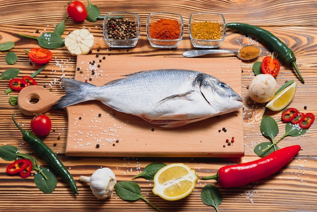 Poisson frais dorado cru sur papier sulfurisé avec du citron, du poivre, des tomates et diverses épices sur une surface en bois avec espace de copie.