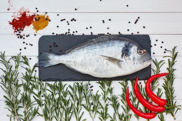 Poisson frais dorado sur planche à découper en ardoise avec romarin, poivron froid sur tableau blanc. Vue de dessus, copie