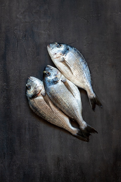 Poisson frais de dorado sur une planche à découper noire sur la table