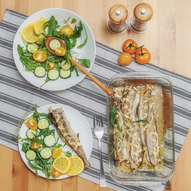 Photo poisson frais frit avec légumes servis sur assiette sur table en bois, vue de dessus