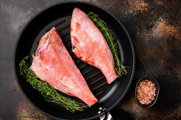 Poisson frais de la perche rouge de l'océan de mer situé dans une poêle en fonte à frire sur un vieux fond de table rustique sombre vue de dessus mise à plat