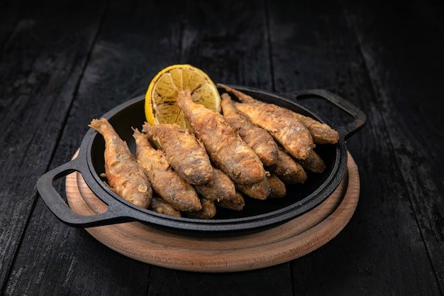 Poisson frit sur une poêle en fonte noire sur une table en bois foncé