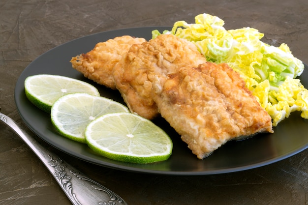 Poisson frit avec de la salade sur une assiette grise.