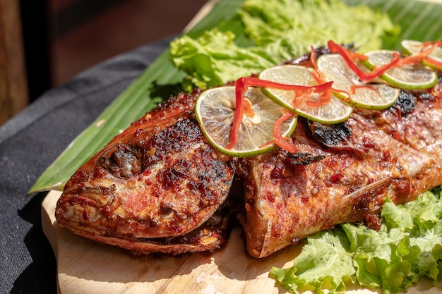 Poisson frit avec salade verte fraîche et citron de Bali Indonésie gros plan Délicieux poisson de mer rôti au citron sur une assiette en bois au restaurant