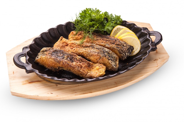 Poisson frit, tranches de poisson frit dans la pâte, servi avec du citron et de la laitue dans une poêle noire sur une planche de bois. fond blanc