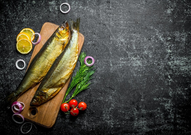 Poisson fumé sur une planche à découper en bois avec tomates aneth et tranches de citron