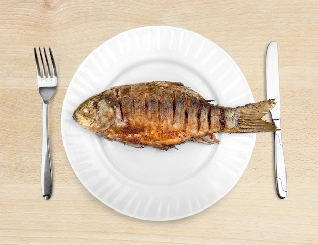 Poisson grillé sur plaque avec fourchette et couteau sur table en bois, vue de dessus