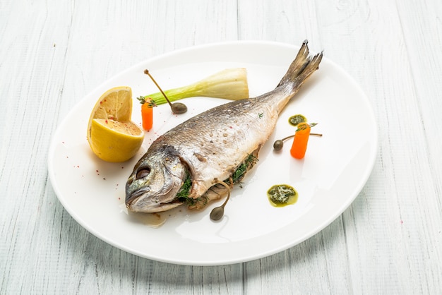 Poisson grillé sur plateau isolé sur blanc. Vue de dessus de la dorade rôtie entière