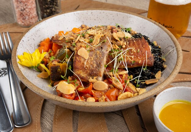 Poisson grillé, riz noir et légumes dans un bol avec sel, poivre, sauce et soda