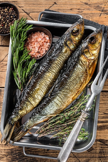 Poisson hareng mariné fumé dans un plateau de cuisine aux herbes. Fond en bois. Vue de dessus.