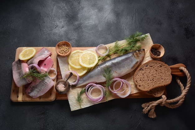 Poisson hareng sur planche de bois avec des herbes de poivre oignon rouge et citron sur fond noir