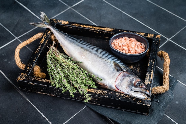 Poisson maquereau cru aux herbes et épices dans un plateau en bois prêt pour la cuisson Fond noir Vue de dessus