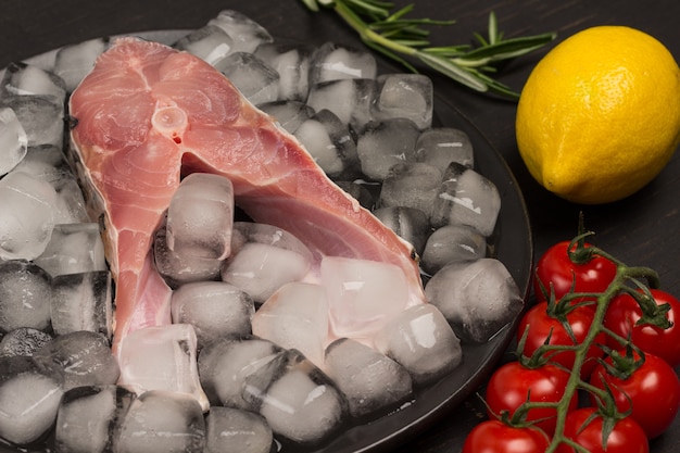 Poisson de rivière frais sur la fonte des glaces sur une plaque en céramique noire. Citron et brin de tomate cerise et romarin.