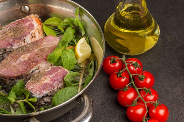 Poisson de rivière haché à la menthe et au romarin dans une poêle. Tomates, bouteille en verre avec de l'huile sur table.