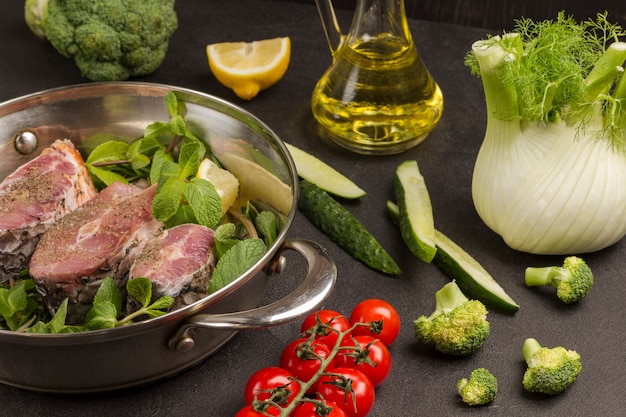 Poisson de rivière haché à la menthe et au romarin dans une poêle. Tomates brocoli et fenouil, concombres, bouteille en verre avec huile