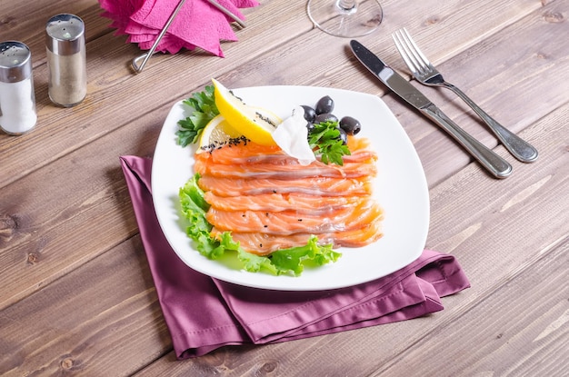 Poisson rouge frais coupé en lanières avec du citron et des herbes sur une plaque blanche sur un fond en bois foncé